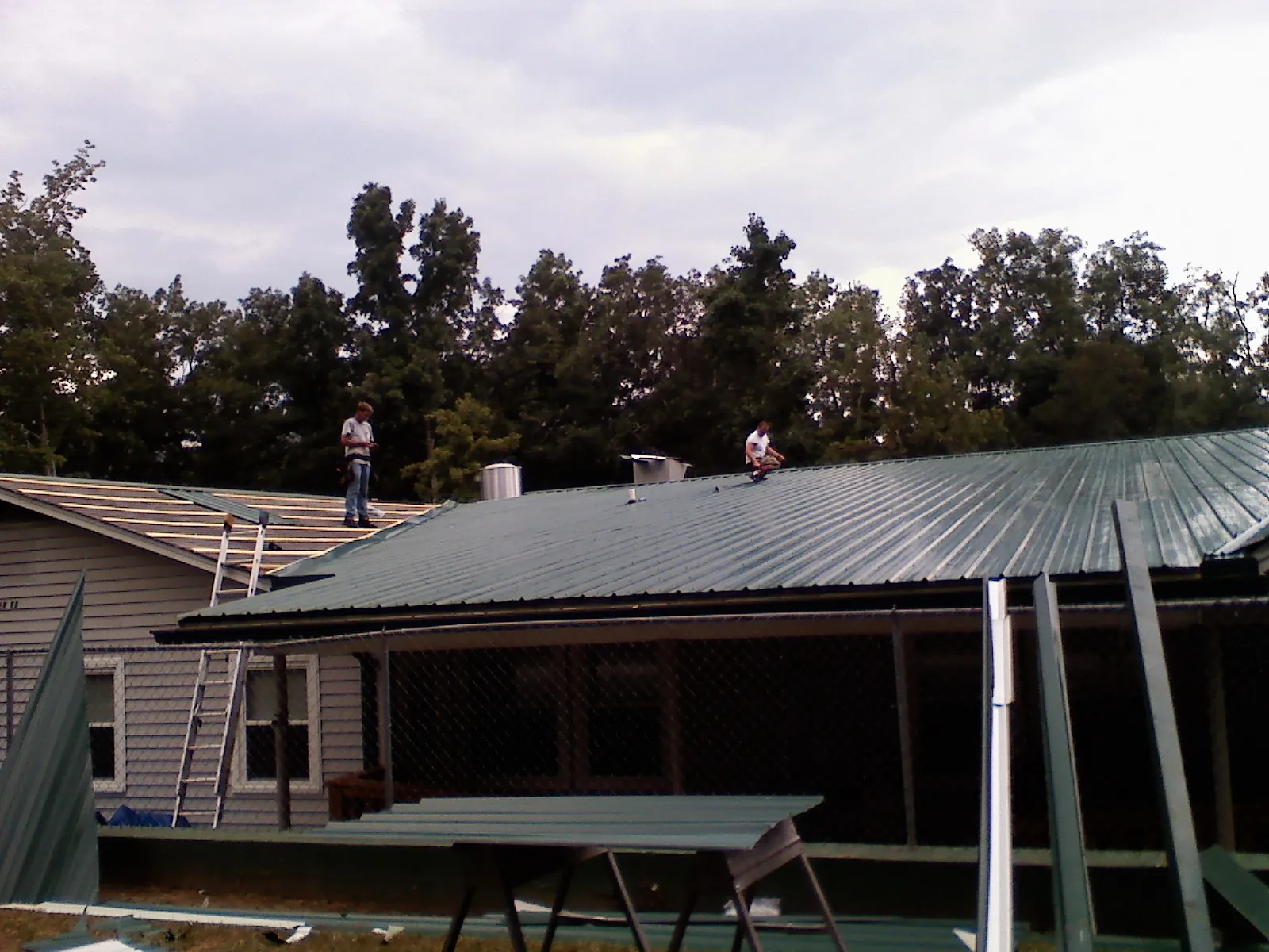 Two roofers installing green metal panels above a covered porch in Piedmont